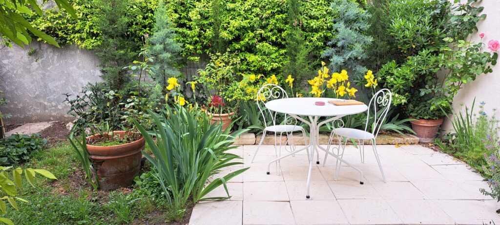 Table et chaises sur la terrasse dans le jardin fleuri de L'Oustau dei Aucèus (vue Ouest N.O.).