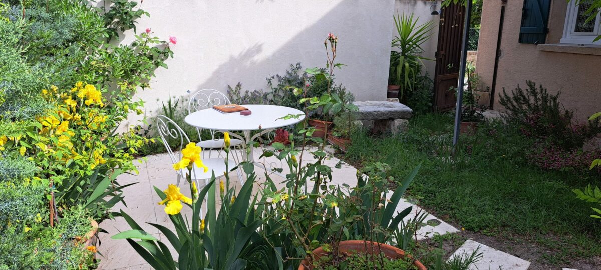Table installée sur la terrasse de L’Oustau dei Aucèus, entourée par les fleurs et la végétation du jardin.