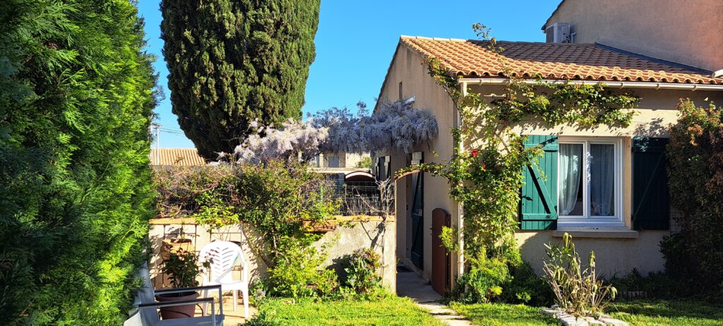 La façade sud de L’Oustau dei Aucèus, fleurie de glycine, avec la porte d’accès privative conduisant vers la piscine extérieure partagée.
