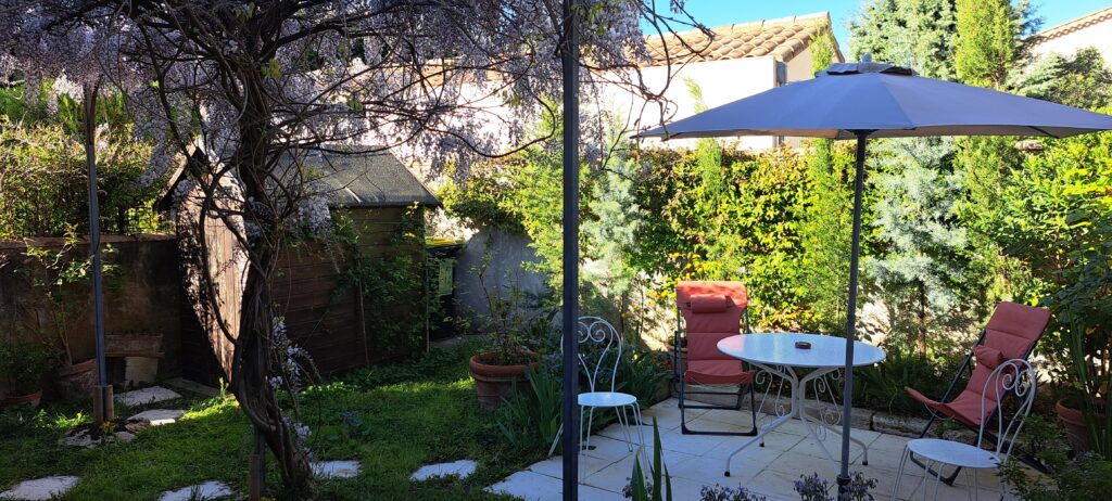 Le jardin privatif et la terrasse de L’Oustau dei Aucèus apparaissent sous la glycine en fleurs, dans un écrin de verdure à Saint-Rémy-de-Provence.