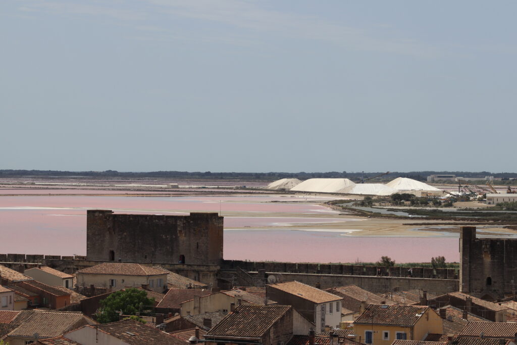 Vue depuis les remparts d’Aigues-Mortes sur les toits de la cité médiévale, les eaux roses du salin et les camelles de sel, à environ 70 km de L’Oustau dei Aucèus.
