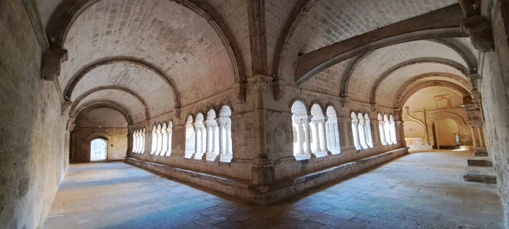 Galerie du cloître roman de l'Abbaye de Montmajour, avec ses voûtes en pierre, ses arcs en plein cintre et ses colonnes ouvrant régulièrement sur la cour centrale.